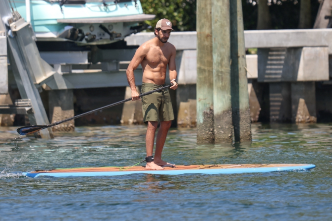 Joaquim Valente  in green shorts and a matching baseball cap while paddleboarding